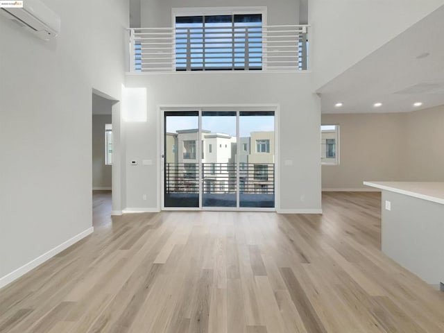 unfurnished living room with light hardwood / wood-style floors, a high ceiling, and a wall mounted AC