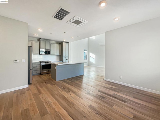 kitchen with a center island with sink, gray cabinets, stainless steel appliances, and hardwood / wood-style floors