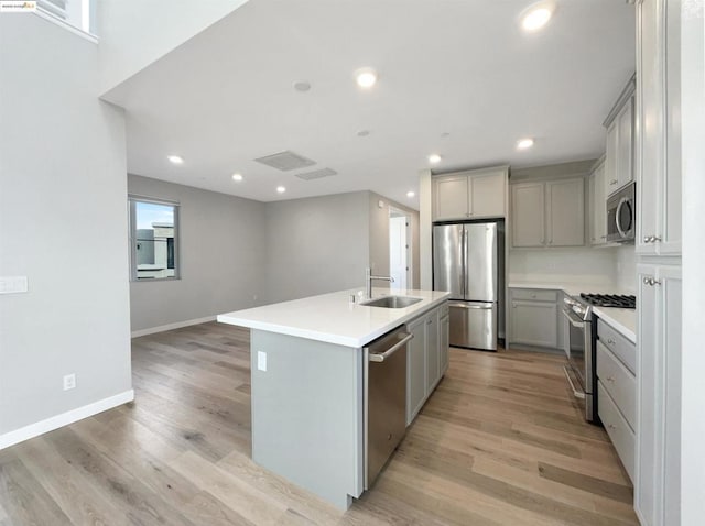 kitchen with light hardwood / wood-style flooring, sink, gray cabinetry, a center island with sink, and stainless steel appliances