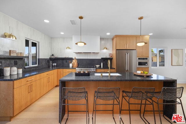 kitchen with hanging light fixtures, an island with sink, appliances with stainless steel finishes, and sink