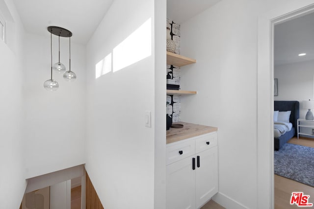 bar featuring light hardwood / wood-style floors, hanging light fixtures, white cabinets, and wooden counters