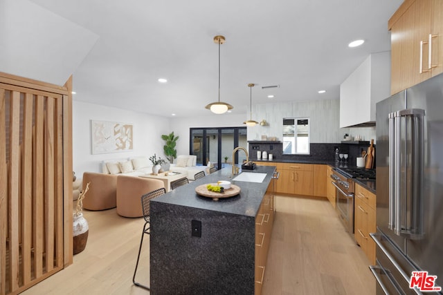 kitchen with decorative light fixtures, decorative backsplash, sink, an island with sink, and high quality appliances