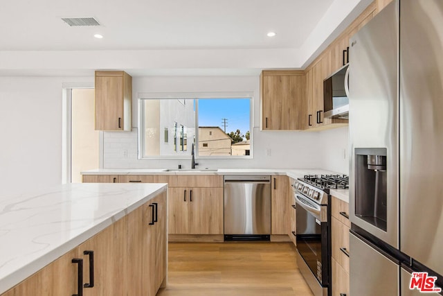 kitchen featuring light brown cabinets, stainless steel appliances, light hardwood / wood-style floors, sink, and light stone counters