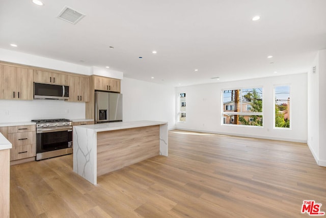 kitchen featuring light wood-type flooring, light brown cabinetry, stainless steel appliances, and a kitchen island