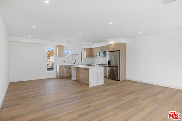 kitchen with light wood-type flooring, appliances with stainless steel finishes, sink, and a center island