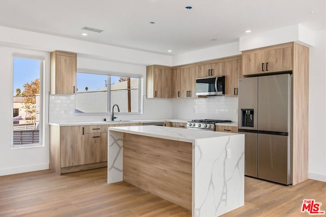 kitchen with light wood-type flooring, appliances with stainless steel finishes, sink, and a center island