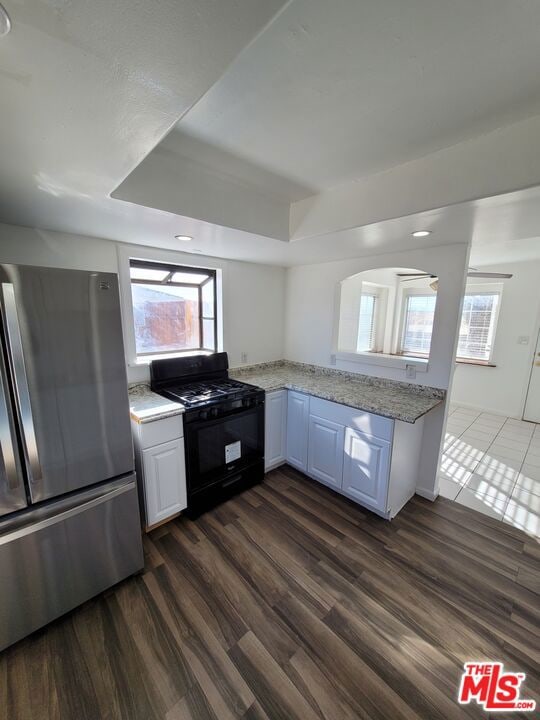 kitchen with dark hardwood / wood-style floors, black gas range, a wealth of natural light, white cabinetry, and stainless steel fridge