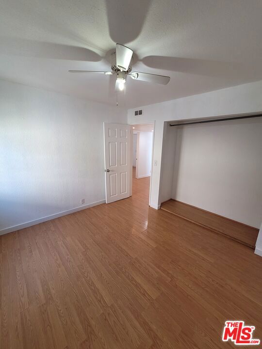 unfurnished bedroom featuring ceiling fan, hardwood / wood-style floors, and a closet