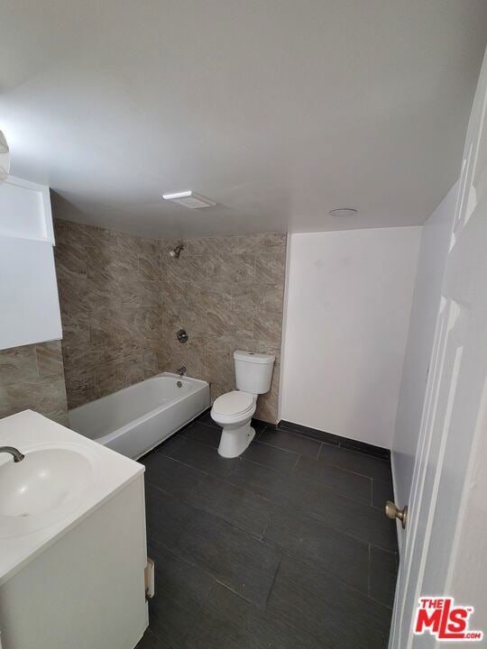 bathroom featuring toilet, tile walls, a tub to relax in, and vanity