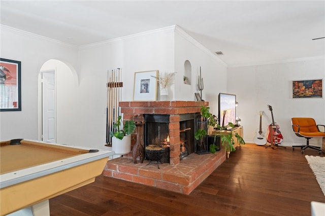 rec room featuring a brick fireplace, dark hardwood / wood-style flooring, and ornamental molding