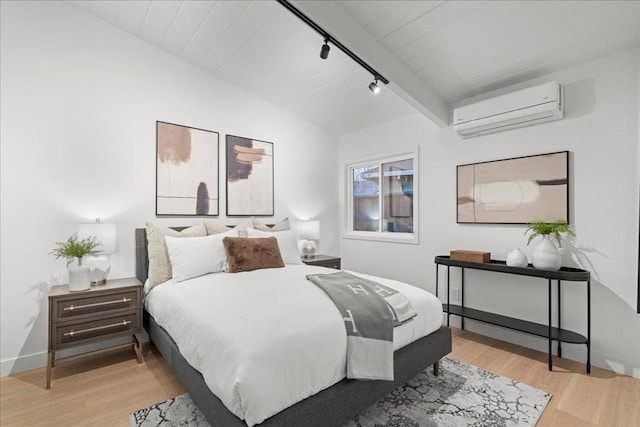 bedroom featuring rail lighting, a wall unit AC, and light hardwood / wood-style flooring