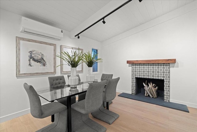 dining area featuring wood-type flooring, rail lighting, a tiled fireplace, and a wall unit AC