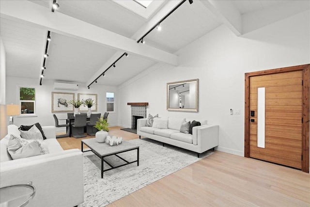 living room featuring an AC wall unit, vaulted ceiling with skylight, a fireplace, track lighting, and light wood-type flooring