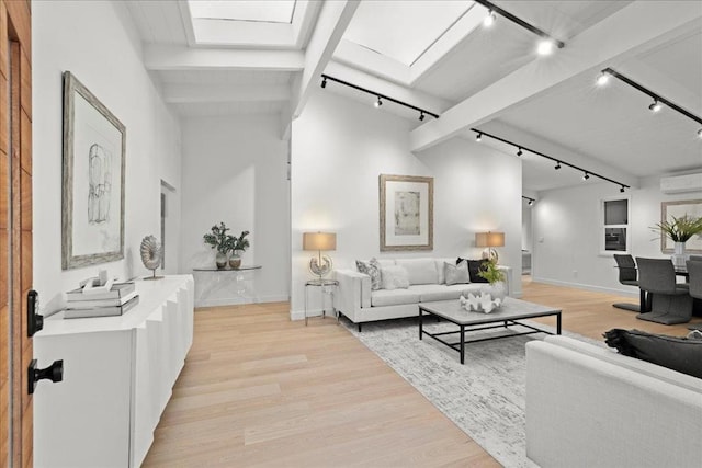 living room featuring rail lighting, lofted ceiling with skylight, a wall mounted AC, and light wood-type flooring