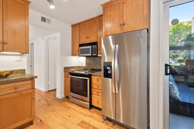 kitchen featuring backsplash, light hardwood / wood-style flooring, stainless steel appliances, and dark stone countertops