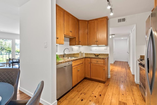 kitchen with sink, dark stone countertops, stainless steel appliances, and light hardwood / wood-style floors