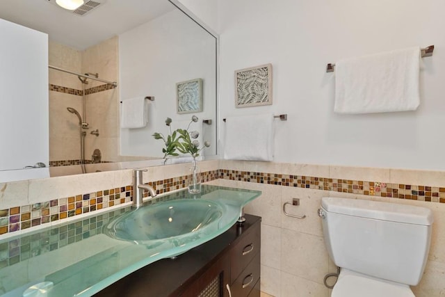 bathroom featuring toilet, vanity, tile walls, and a tile shower