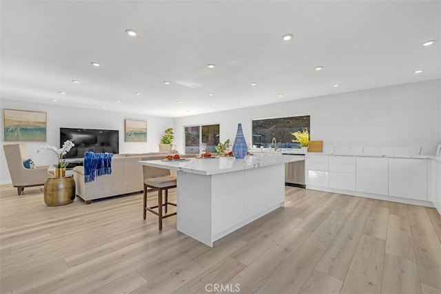 kitchen with white cabinetry, light hardwood / wood-style flooring, a breakfast bar, and a spacious island