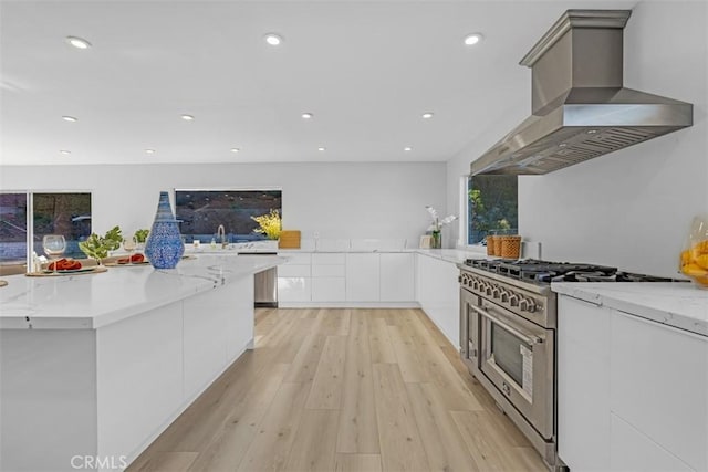 kitchen featuring island range hood, white cabinets, stainless steel range, light stone counters, and light hardwood / wood-style flooring