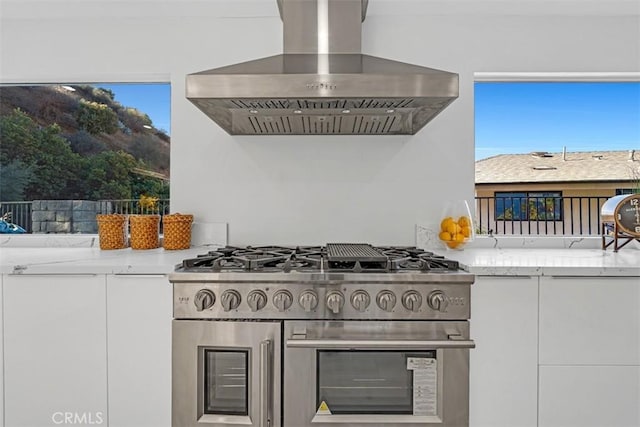 kitchen with white cabinetry, island range hood, light stone counters, and high end stove