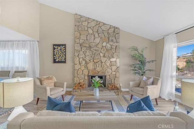 living room with a stone fireplace, light hardwood / wood-style floors, and vaulted ceiling