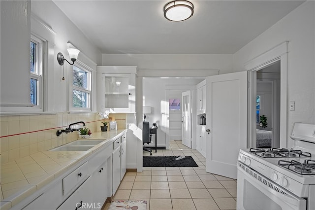 kitchen featuring tile countertops, sink, white cabinetry, white range with gas stovetop, and light tile patterned floors