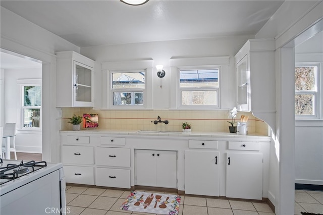 kitchen featuring light tile patterned floors, white cabinetry, tile counters, backsplash, and sink