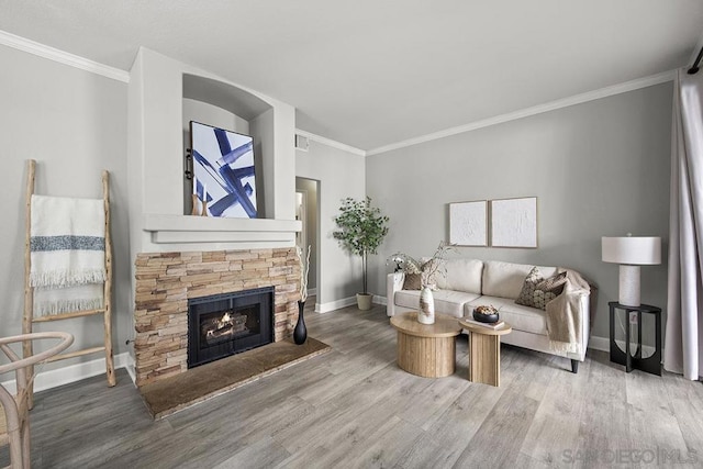 living room with crown molding, a stone fireplace, and light hardwood / wood-style flooring