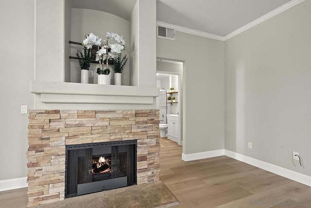 details with ornamental molding, hardwood / wood-style flooring, and a stone fireplace