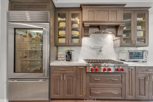 kitchen with stainless steel appliances, decorative backsplash, light stone counters, and wall chimney range hood