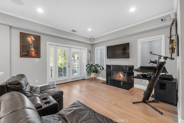 living room featuring wood-type flooring, a tile fireplace, crown molding, and french doors