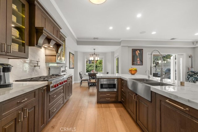 kitchen featuring backsplash, hanging light fixtures, light wood-type flooring, light stone counters, and stainless steel gas stovetop