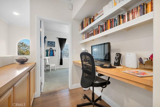 office space with built in desk, light wood-type flooring, and crown molding