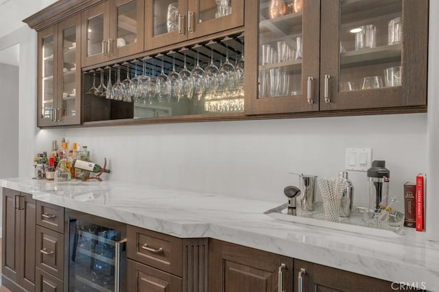 bar featuring wine cooler, light stone countertops, and dark brown cabinetry