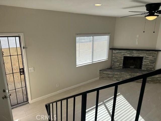 unfurnished living room with ceiling fan and a stone fireplace