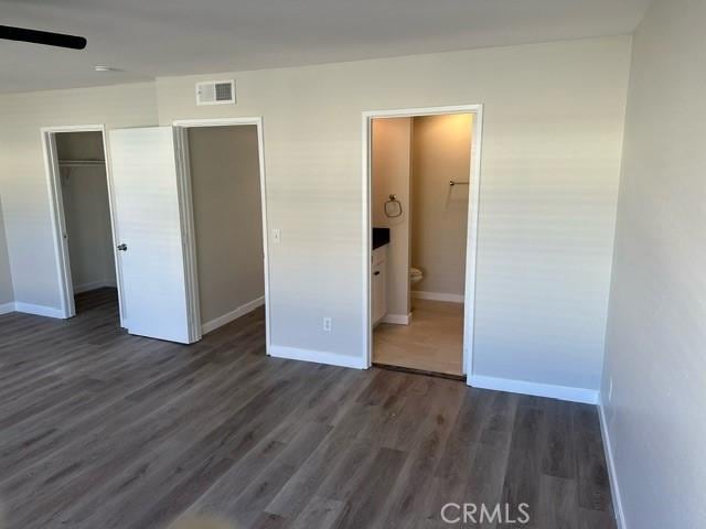 unfurnished bedroom with ensuite bathroom, a walk in closet, a closet, and dark wood-type flooring