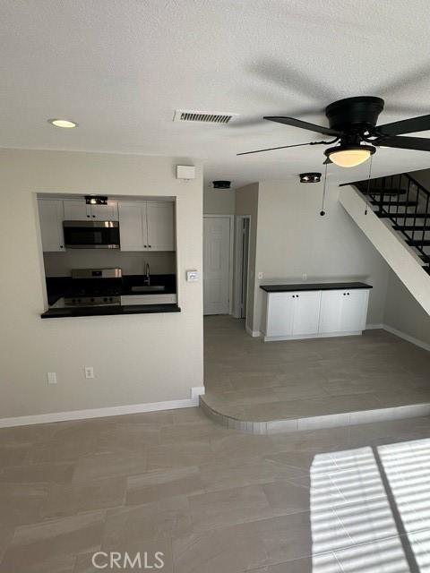 unfurnished living room featuring a textured ceiling, ceiling fan, light tile patterned floors, and sink