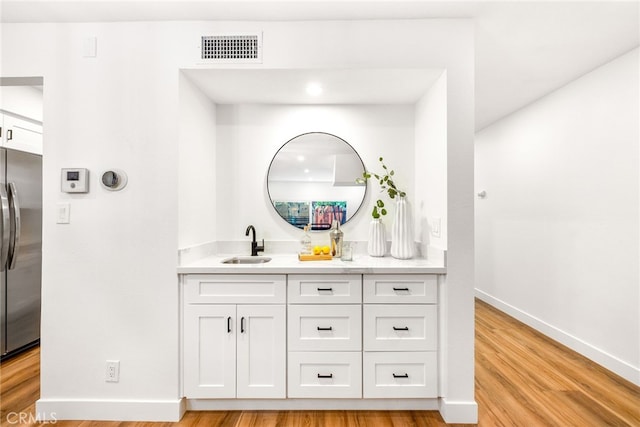 bathroom with visible vents, vanity, baseboards, and wood finished floors