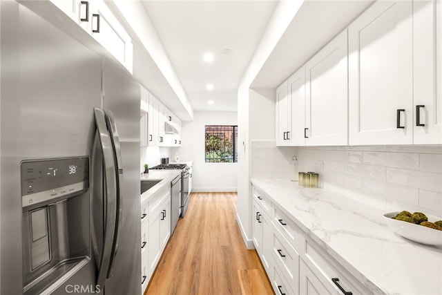 kitchen featuring white cabinets, appliances with stainless steel finishes, light wood-type flooring, decorative backsplash, and light stone countertops