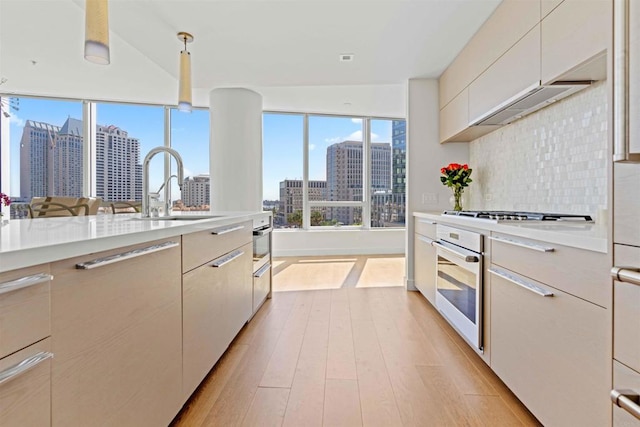 kitchen featuring pendant lighting, stainless steel appliances, decorative backsplash, sink, and light hardwood / wood-style flooring