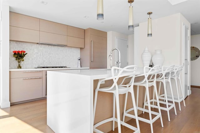 kitchen featuring light brown cabinets, sink, backsplash, hanging light fixtures, and light wood-type flooring