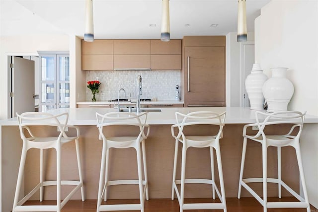 kitchen with decorative backsplash, light brown cabinetry, sink, and a breakfast bar area