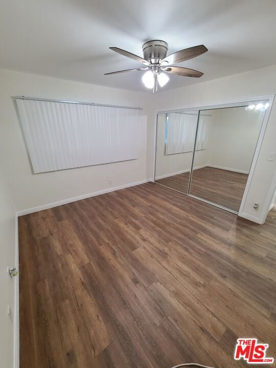 unfurnished bedroom featuring ceiling fan, a closet, and dark wood-type flooring