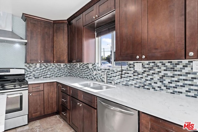 kitchen featuring appliances with stainless steel finishes, tasteful backsplash, dark brown cabinets, wall chimney range hood, and sink