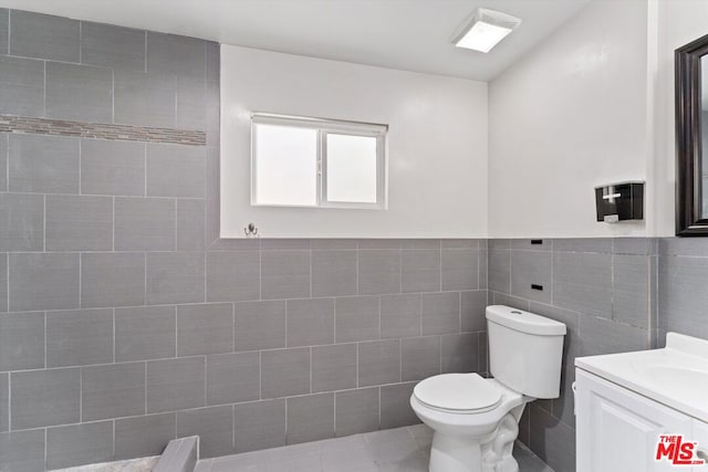 bathroom with tile walls, toilet, vanity, and tile patterned flooring