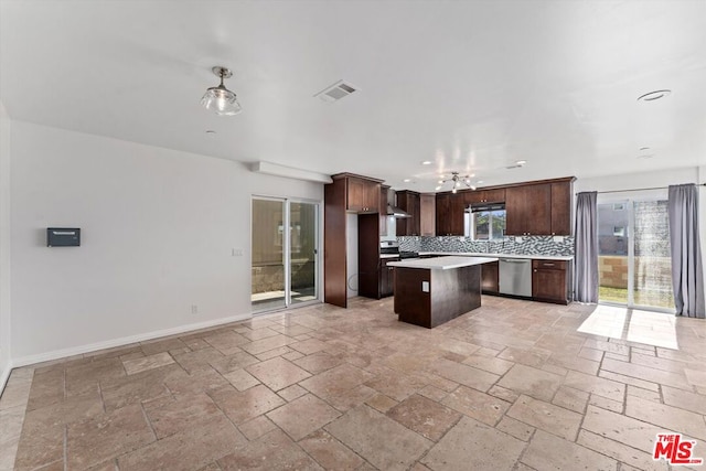 kitchen with appliances with stainless steel finishes, a kitchen island, wall chimney range hood, decorative backsplash, and dark brown cabinets