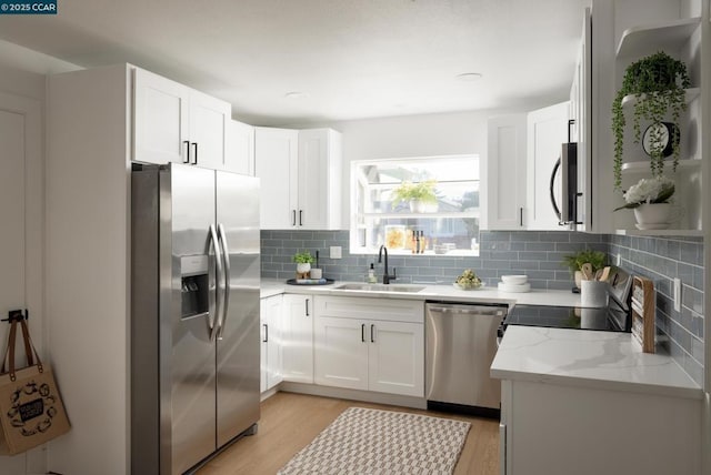 kitchen with light stone countertops, white cabinetry, stainless steel appliances, sink, and light hardwood / wood-style flooring