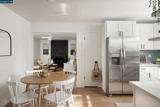 kitchen with a fireplace, stainless steel fridge with ice dispenser, white cabinetry, light hardwood / wood-style flooring, and backsplash