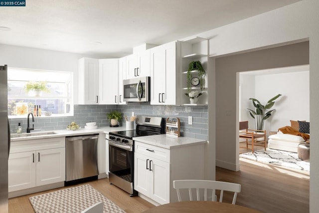 kitchen with light hardwood / wood-style floors, appliances with stainless steel finishes, white cabinetry, decorative backsplash, and sink