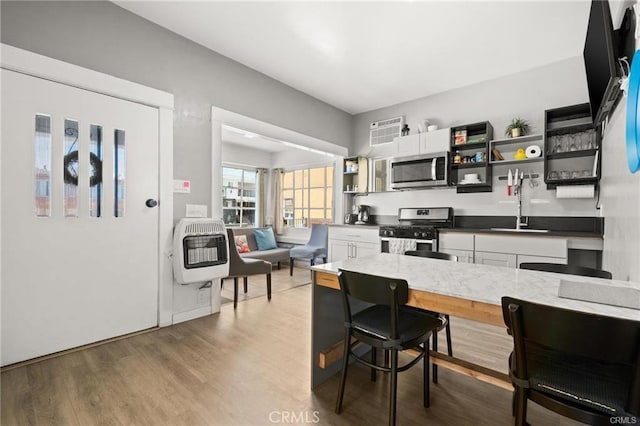 kitchen with sink, white cabinetry, hardwood / wood-style flooring, heating unit, and stainless steel appliances